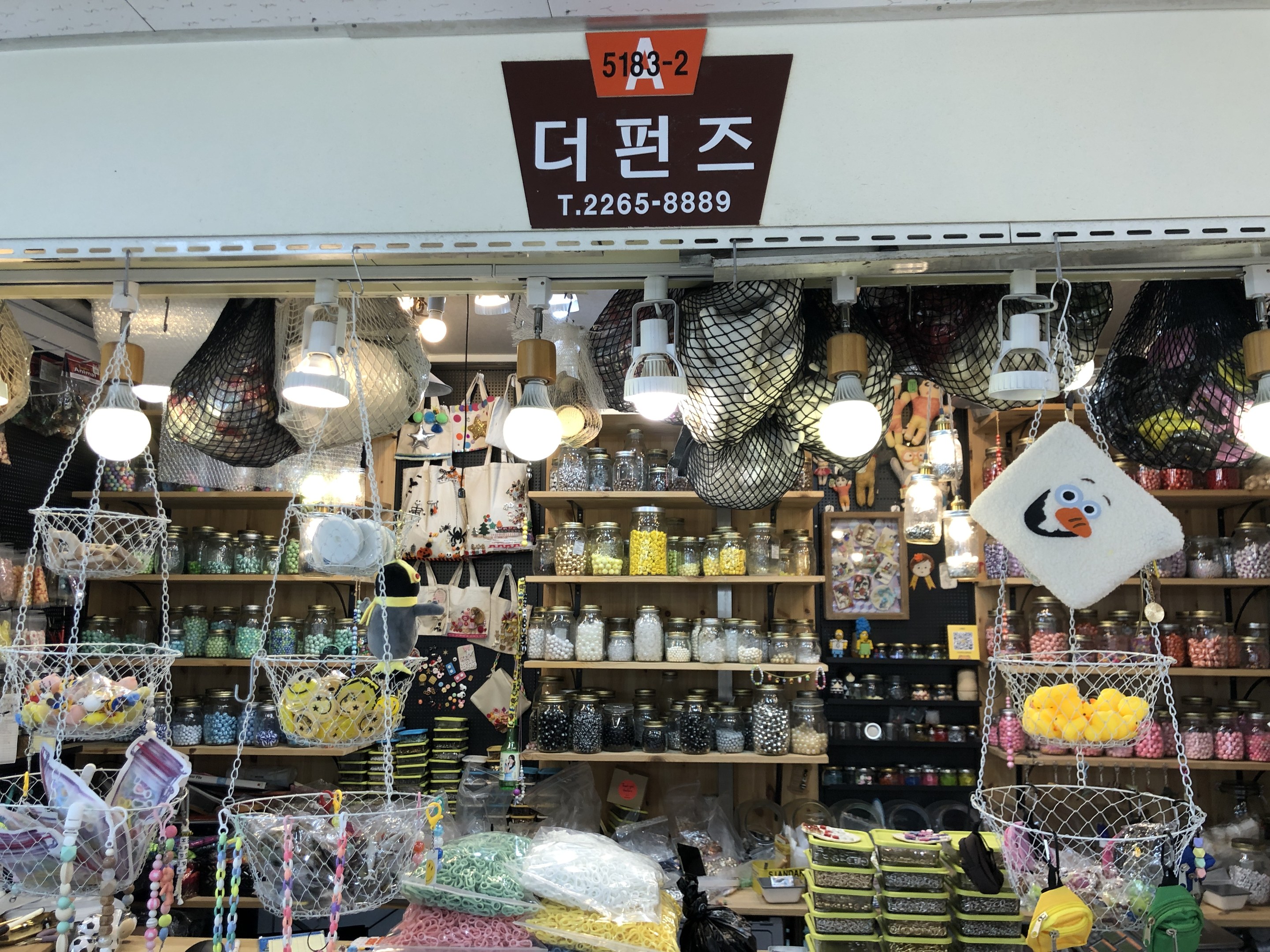 Ein unordentlicher Laden in Seoul zeigt verschiedene Gegenstände wie Körbe, Lampen, Flaschen und Spielzeuge auf Regalen, mit einer Tafel oben, die ihn als einen der besten koreanischen Läden kennzeichnet.