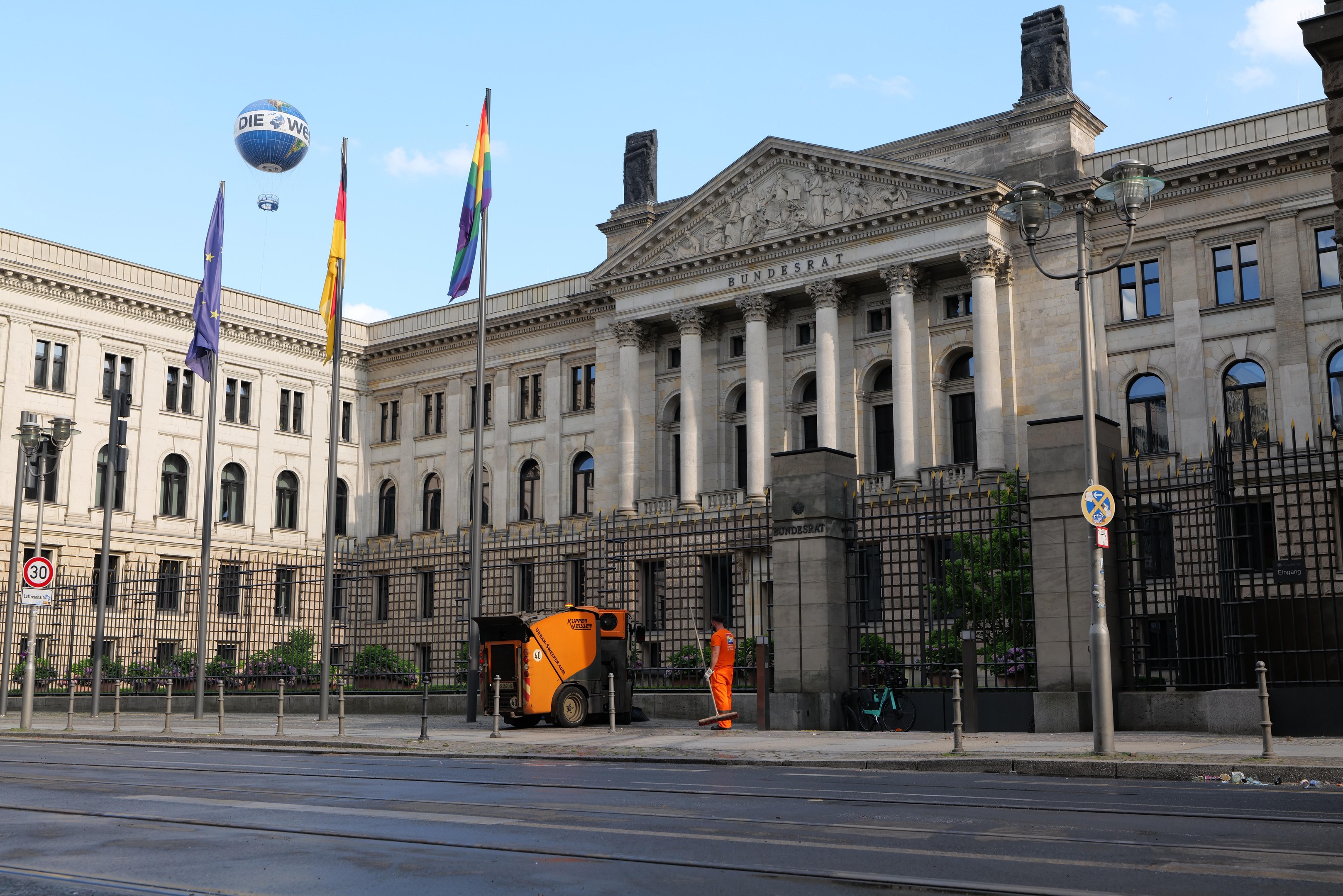 Großes modernes Gebäude mit vielen Fenstern, als Bundestag in Berlin, Deutschland identifiziert, umgeben von Straßeninfrastruktur und Fußgängern unter einem bewölkten Himmel.
