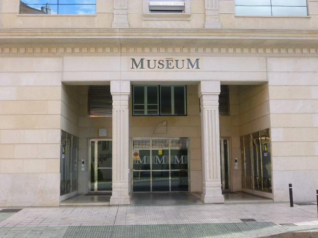 Gro├čes Geb├Ąude mit Glasfenstern und -türen, Pfeilern und Wandtext, mit einem Weg, der zur Museums├Ąnterung führt.