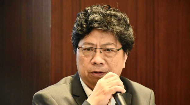 Ein Mann in Anzug und Krawatte hält ein Mikrofon gegen eine hölzerne Wand, Bezug nehmend auf die Suspendierung der Philippinen vom Gericht wegen COVID-19-Beteiligung.