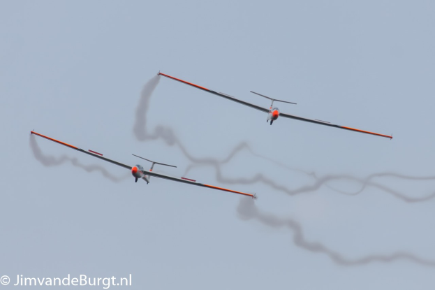 Zwei Segelflugzeuge am Himmel mit Rauchspuren, mit Text in der linken unteren Ecke.