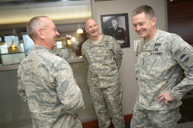 Drei uniformierte Männer, die vor einer Wand mit einem Foto Rahmen, einem Glasfenster mit Laternen und Tischen und einer braunen Tür auf der rechten Seite stehen und lächeln.