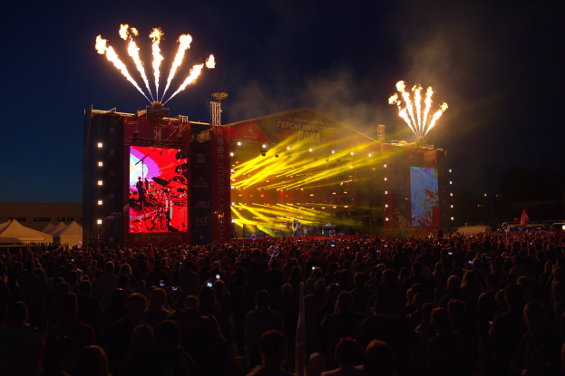 Große Menschenmenge auf einem Musikfestival mit beleuchteter Bühne und Feuerwerk am dunklen Himmel.