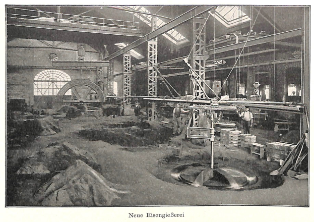 Schwarze und weiße Fotografie eines Fabrikgebäudes mit Arbeitern an Maschinen, umgeben von Metallstangen und -pfosten, beschriftet mit "Neue Eisenglebeerei, die erste Fabrik Deutschlands" unten.