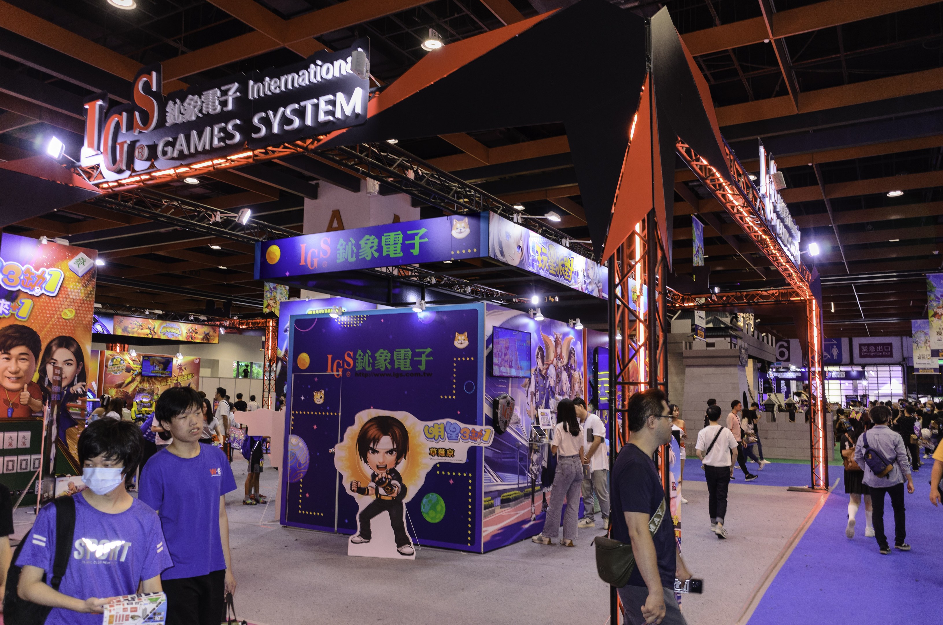 Menschen gehen durch einen Convention Hall auf einer Gaming-Messe in China, einige tragen Taschen und halten Gegenstände, mit Text- und Bildtafeln, Deckenleuchten und Teppichboden.