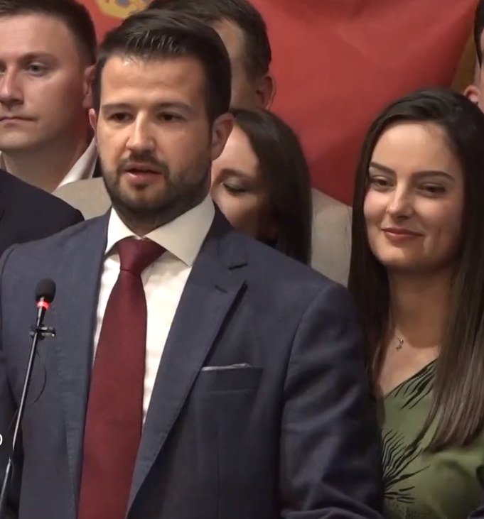 Ein Mann in Anzug und Krawatte spricht an einem Podium mit Mikrofon zu einer Menge hinter einem Banner, wahrscheinlich als Reaktion auf ein Regierungssozialmedienverbot.