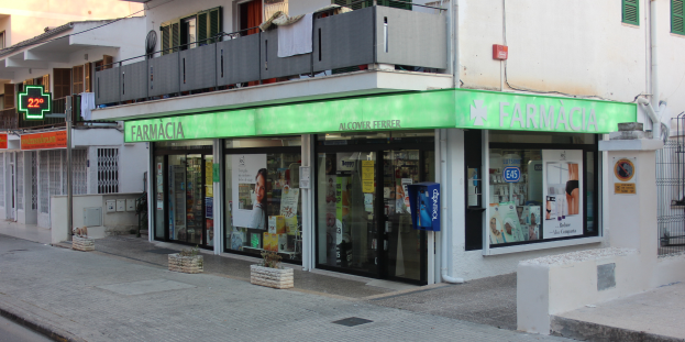 Eine Apotheke an einer Straßenecke mit Gebäuden, Geschäften, Schildern, Strommasten, Kabeln, Kraftfahrzeugen, Topfpflanzen und einem klaren blauen Himmel.