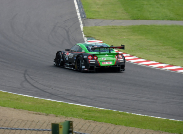 Ein Nissan GT-R Nismo GT3 Rennauto auf der Nürburgring 24 Stunden Strecke, umgeben von grünem Gras und einem Zaun unten.