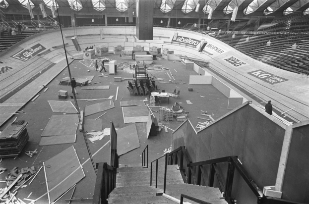 Schwarzes und weißes Foto eines großen Stadions mit verstreuter Trümmer, darunter Treppen, Geländer, Pfosten und Bretter, sowie einigen anwesenden Menschen und der sichtbaren Decke.