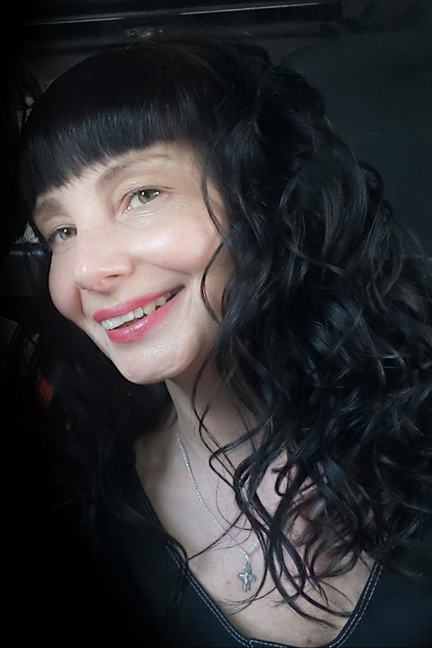 Eine strahlende Frau mit langen schwarzen Haaren und Pony, deren Gesicht von ihren Haaren umrahmt wird, strahlt Wärme und Freude aus.