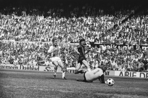 Schwarzes Foto von Fussballspielern im Einsatz mit Zuschauern im Hintergrund und einer Bundesliga 1978-79 Ajax 1-1 Hannover 96 Fahne.