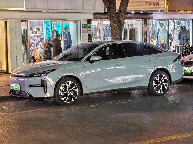 Ein Mitsubishi Lancer EV, der nachts auf einer Straße geparkt ist, umgeben von Gebäuden, Geschäften, Schaufensterpuppen, Schildern und Lichtern.