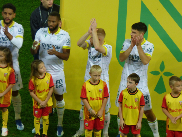 Gruppe von Füßtballspielern in Uniformen, die auf einem Feld mit einem "Ligue 1"-Schild im Hintergrund klatschen und einen Sieg feiern.