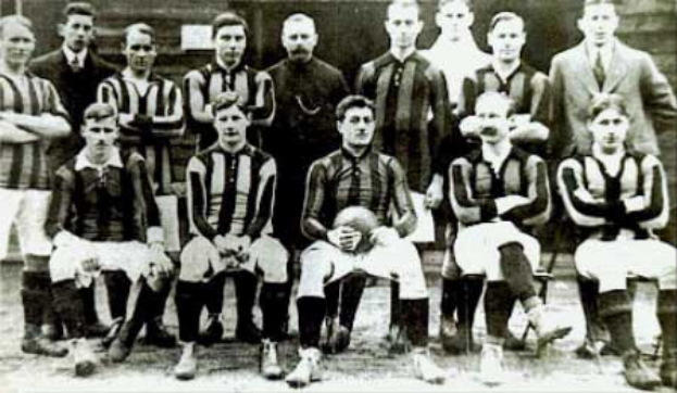 Ein Schwarz-Weiß-Foto einer Fussballmannschaft, wobei einige stehen und einige sitzen, vor einer Wand, mit dem Text "Ballymena Football Club" unten.