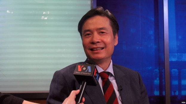 Ein Mann im Anzug hält ein Mikrofon und spricht hinein, während links die Hand eines Reporters zu sehen ist und ein Fenster im Hintergrund.