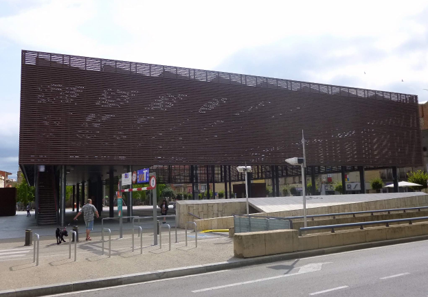 Großes modernes Gebäude mit zahlreichen Fenstern als neuer Eingang zur City, flankiert von Straßeninfrastruktur und städtischer Aktivität.