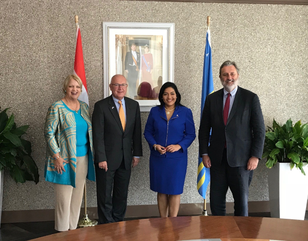 Gruppe von Menschen, die um einen Tisch mit Papieren stehen, umgeben von Fahnen, Topfpflanzen und einem Rahmenfoto an der Wand, was die Unterzeichnung eines U.S.-Kanada-Memorandums von Verständigung anzeigt.