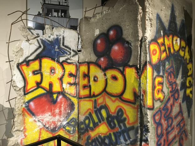 Eine Wand mit Graffiti, das in großen schwarzen Buchstaben 'Freiheit und Demokratie' lautet, ein Geländer unten und ein Gebäude mit Fenstern im Hintergrund.
