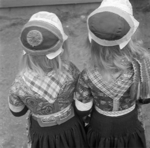 Zwei junge Mädchen in traditionellen bayrischen Kleidern und Hüten stehen nebeneinander vor einer Wand in einem Schwarz-Weiß-Foto.