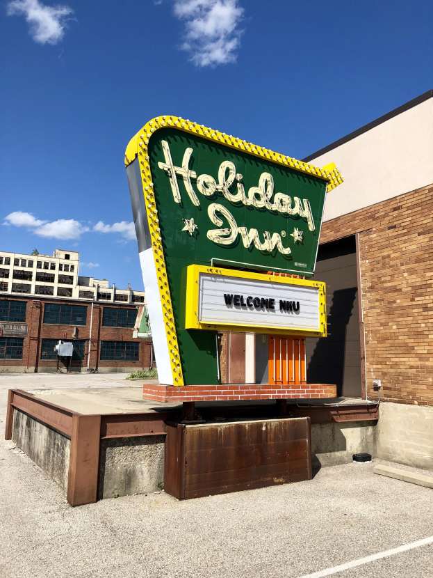 Holiday Inn Schilder auf einem Gebäude mit einem Wegweiser vorne, bewölkter Himmel im Hintergrund.