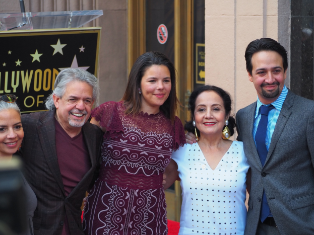 Gruppe von Menschen auf einem roten Teppich bei der Zeremonie des Hollywood Walk of Fame, mit einer Tafel, Glaspodest und Wand im Hintergrund.