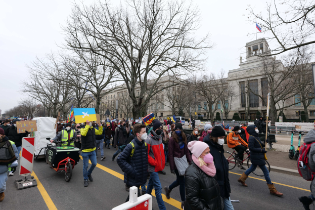 Eine große Gruppe von Menschen marschiert bei einer Demonstration auf einer Straße in Washington, D.C., mit Schildern, Bannern und Fahrrädern unter einem klaren blauen Himmel.