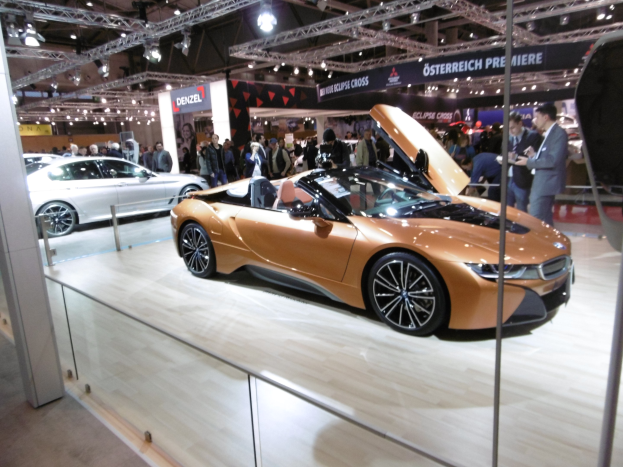 Ein schicker schwarzer BMW i8 Roadster mit Chromakzenten auf der Frankfurt Motor Show umgeben von formell gekleideten Gästen in einer Atmosphäre der Aufregung.