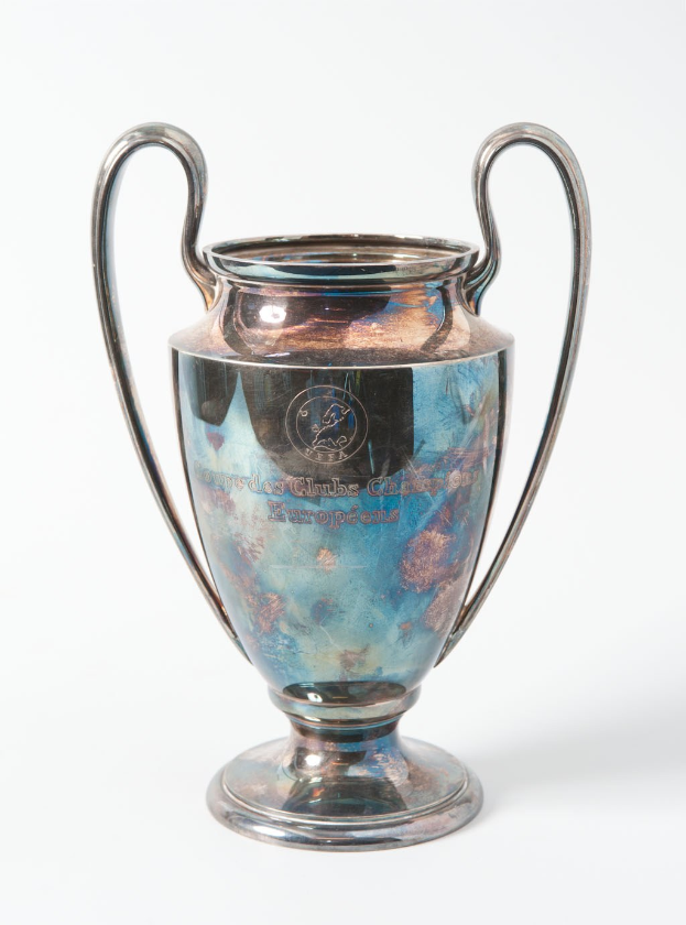 Der UEFA Champions League-Pokal, ein stahlerner Becher mit zwei Griffen und einem blauen und silbernen Farbschema, mit der Inschrift "UEFA Champions League" auf einem weißen Hintergrund.