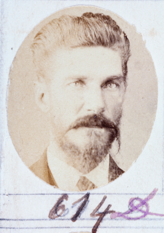 Ein altes Foto eines Mannes mit ordentlich gekämmtem Haar, vollem Bart und Schnurrbart, der direkt in die Kamera schaut.