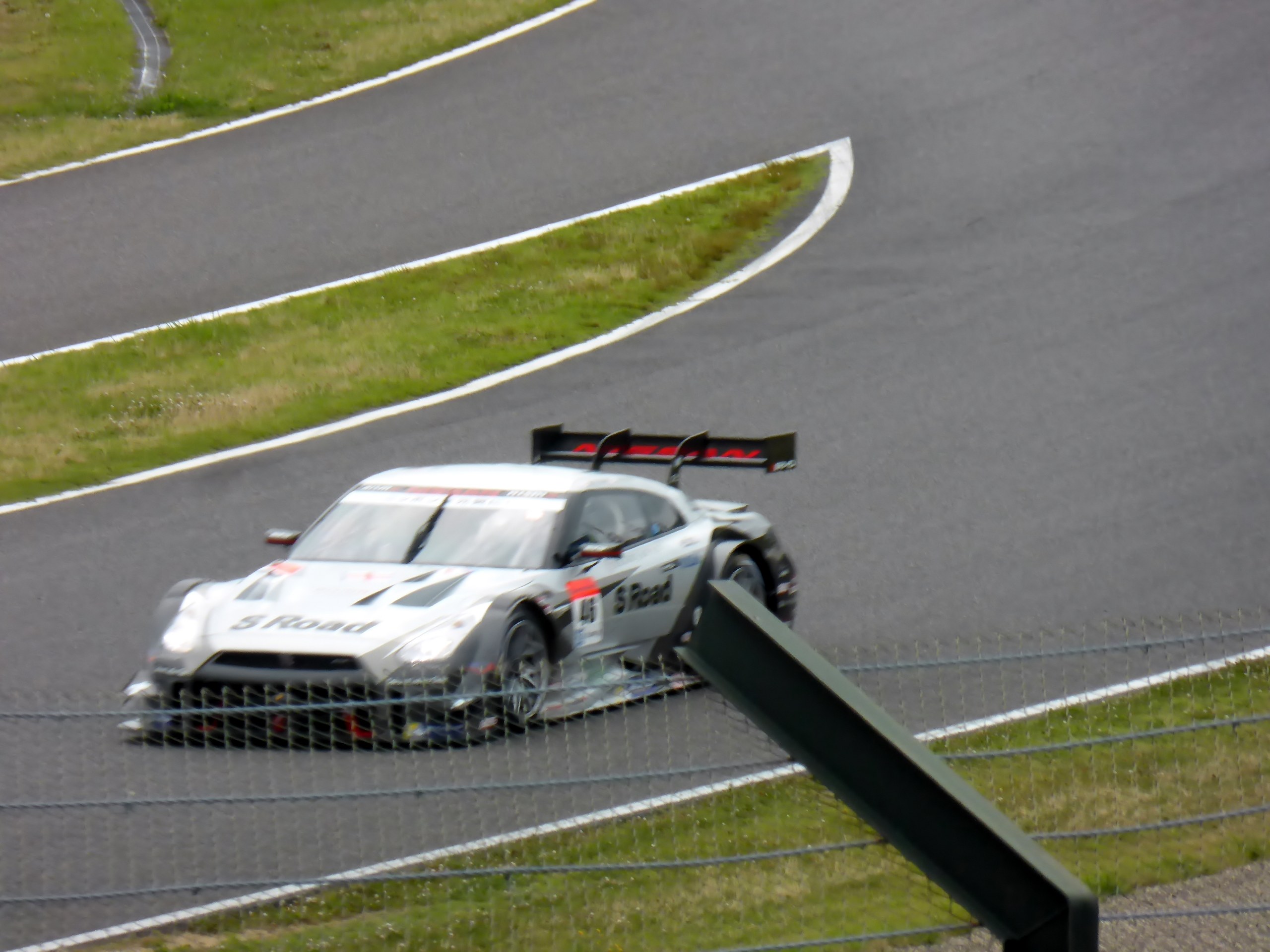 Audi R8 LMS GT3 auf der Nürburgring 24 Stunden Rennstrecke, umgeben von einem Metallzaun und saftigem Grün, mit der Strecke, die vor dem Auto verläuft.