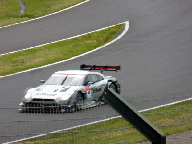 Audi R8 LMS GT3 auf der Nürburgring 24 Stunden Rennstrecke, umgeben von einem Metallzaun und saftigem Grün, mit der Strecke, die vor dem Auto verläuft.