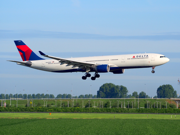 Ein Boeing 787-9 Dreamliner der Delta Air Lines startet vom Frankfurter Flughafen, mit grünem Gras, Laternen, Bäumen, einem Turm auf der rechten Seite und weißen Wolken am Himmel.
