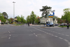 Eine Kreisverkehrausfahrt mit einem parkenden Polizeiwagen, fahrenden Fahrzeugen, Fußgängern auf dem Gehweg, Verkehrsampeln, Bäumen, Gebäuden mit Fenstern und einem bewölkten Himmel.