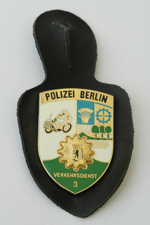 Ein schildförmiges Polizeibadge mit der Aufschrift 'Polizei Berlin' auf blauem Hintergrund, weißem Rand und einem zentralen weißen Stern, das auf einer Oberfläche liegt.