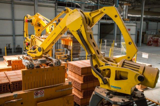 Ein großes Lager mit zahlreichen Kisten, Kränen, einem Zaun, Pfählen und anderem industriellen Equipment, mit einer Wand im Hintergrund.