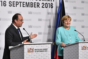 Bundeskanzlerin Angela Merkel und Frankreichs Präsident François Hollande stehen vor zwei Podien mit Mikrofonen, beide lächeln, mit einem "Bratislava-Gipfel 2016"-Schild dahinter.