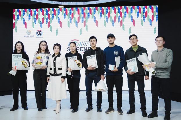 Eine Gruppe von Menschen auf einer Bühne mit Bücher und Blumensträußen in den Händen, im Hintergrund ein Bildschirm mit der Aufschrift "Yogyakarta International School of Science and Technology".