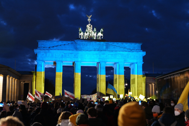 Eine Menschenmenge steht vor dem Brandenburger Tor in Berlin, Deutschland, mit Fahnen und Plakaten in den Händen, mit einer Banner auf der rechten Seite des Bildes.