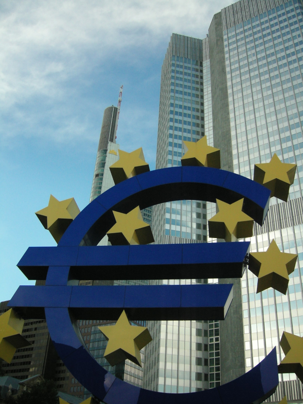Euro-Zeichen vor dem Hauptquartier der Europäischen Zentralbank in Frankfurt, Deutschland, mit umliegenden Bäumen und bewölktem Himmel.